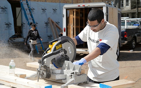 Travelers volunteer using saw to cut wood at volunteer site