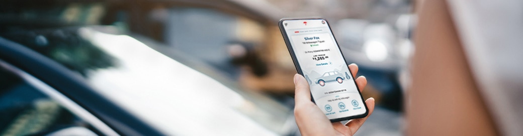 Woman holding mobile phone displaying MyTravelers app, car in background.