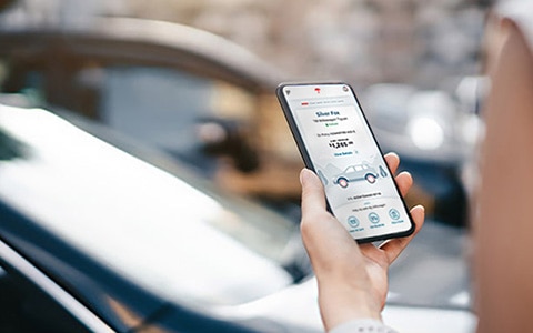 Woman holding mobile phone displaying MyTravelers app, car in background