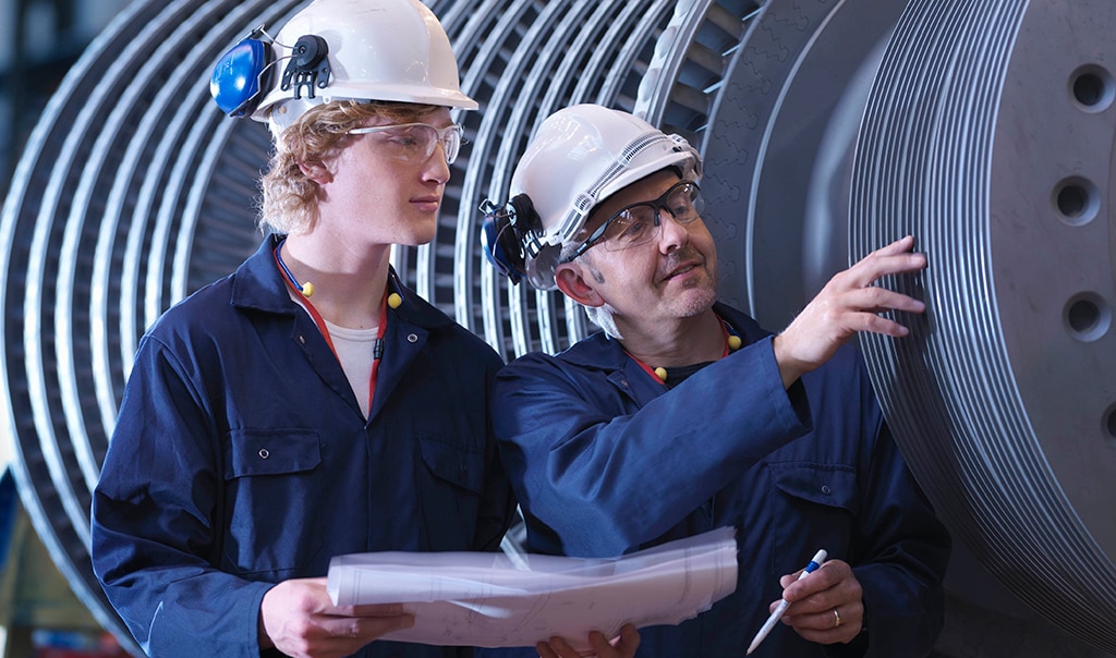 Two engineers having a meeting and inspecting a huge machine with layers of discs.