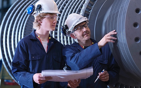 Two engineers having a meeting and inspecting a huge machine with layers of discs.