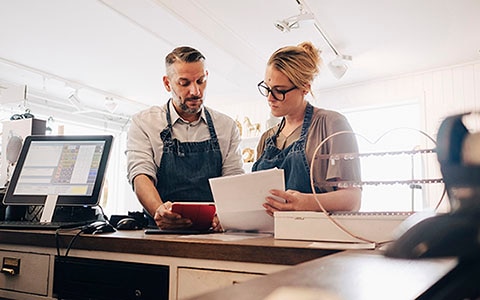 Two People in denim aprons reviewing information on ipad and papers