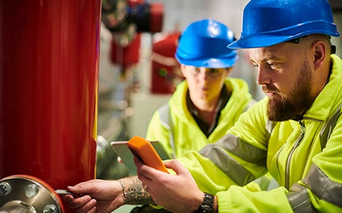 Two People in hard hats inspecting pipes and valves