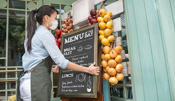 woman sets sign outside her shop wearing a mask, reopening your shop or restaurant as the pandemic evolves