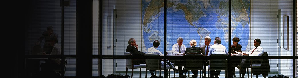 a group of business people around a conference table with a map of the world in the background