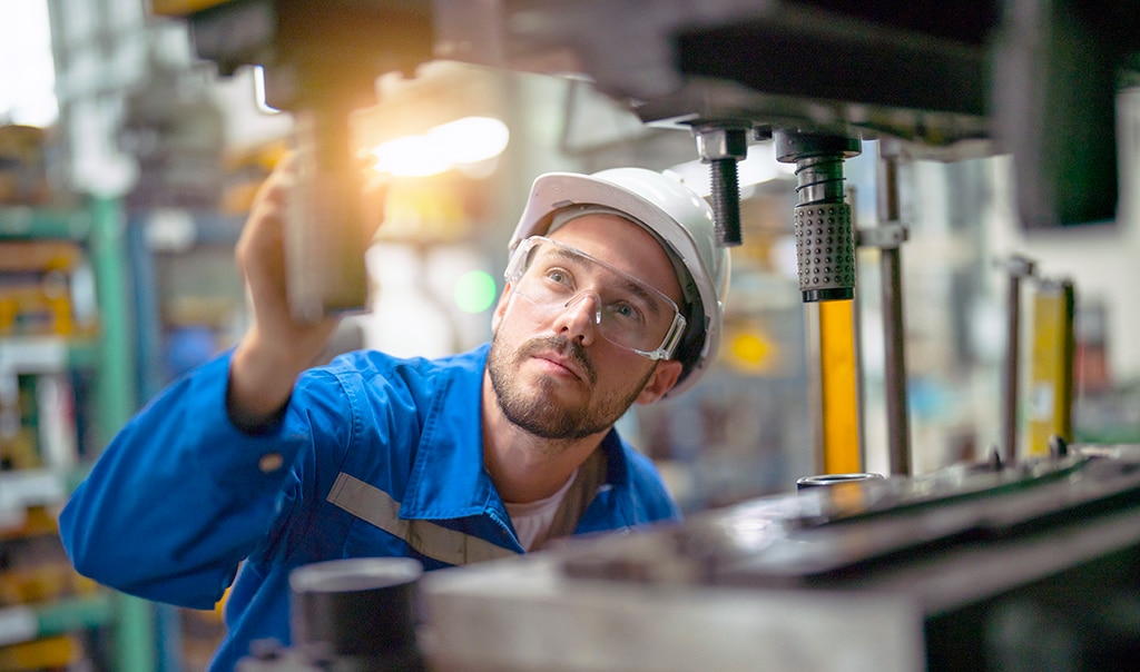A man in safety equipment analyzing a machine for possible breakdown