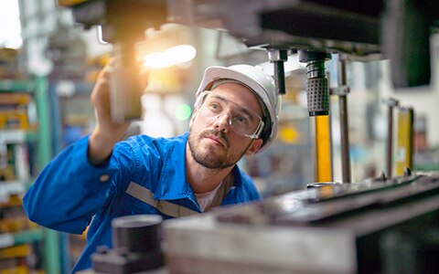 A man in safety equipment analyzing a machine for possible breakdown