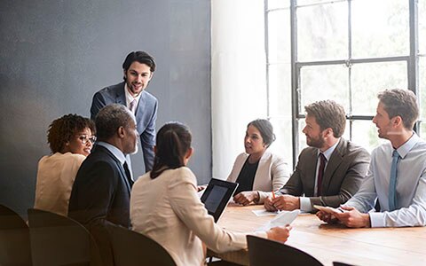 Group of 7 agents in suits sitting around table looking at person talking