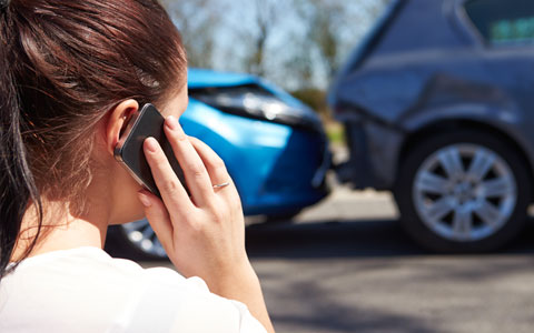 woman talking on her phone as she looks at car accident 