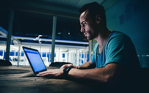 man sitting in a dark room looking at a laptop computer
