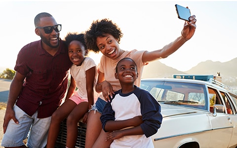 Family taking a selfie in front of a car.