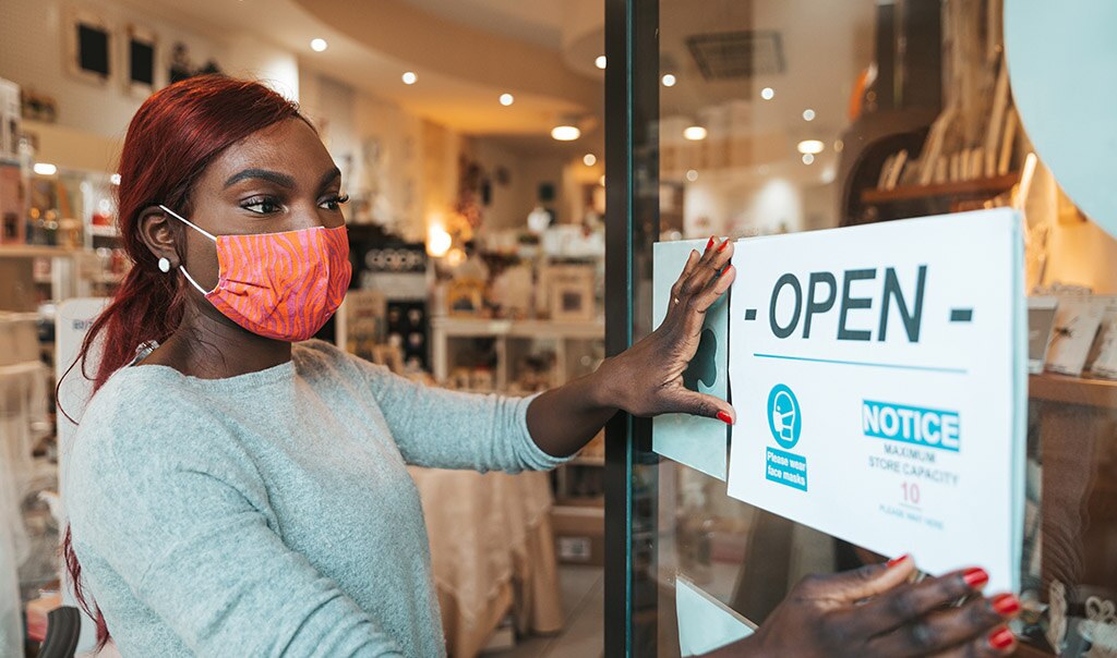 Woman wearing mask placing open sign up at front of business