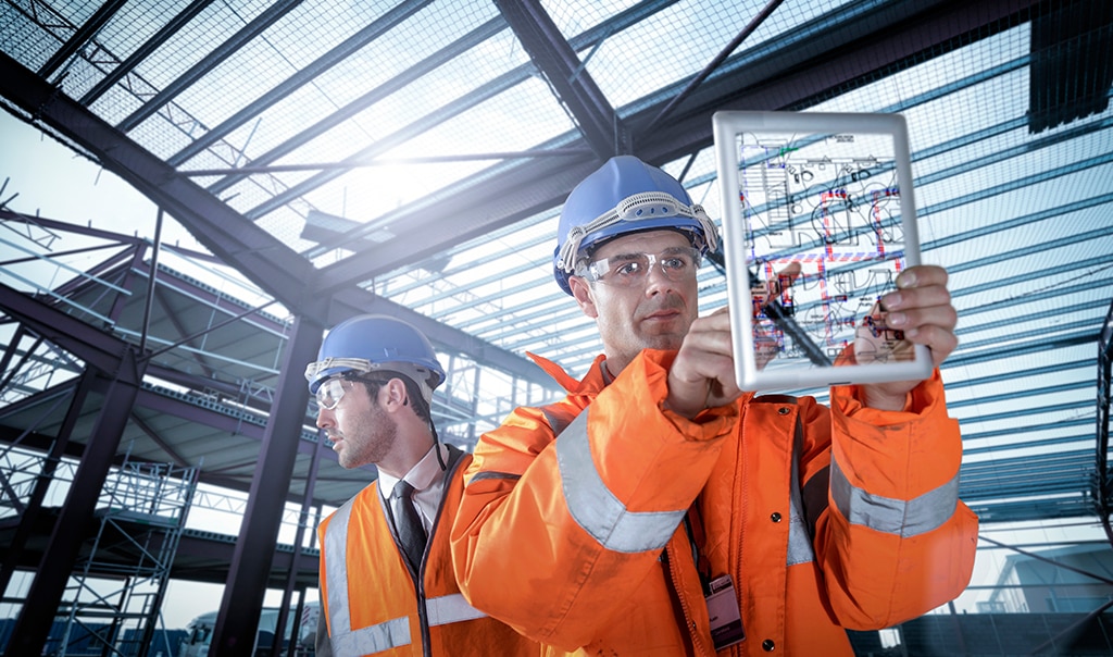 Two male construction workers on site inspecting and one of them touching a tablet