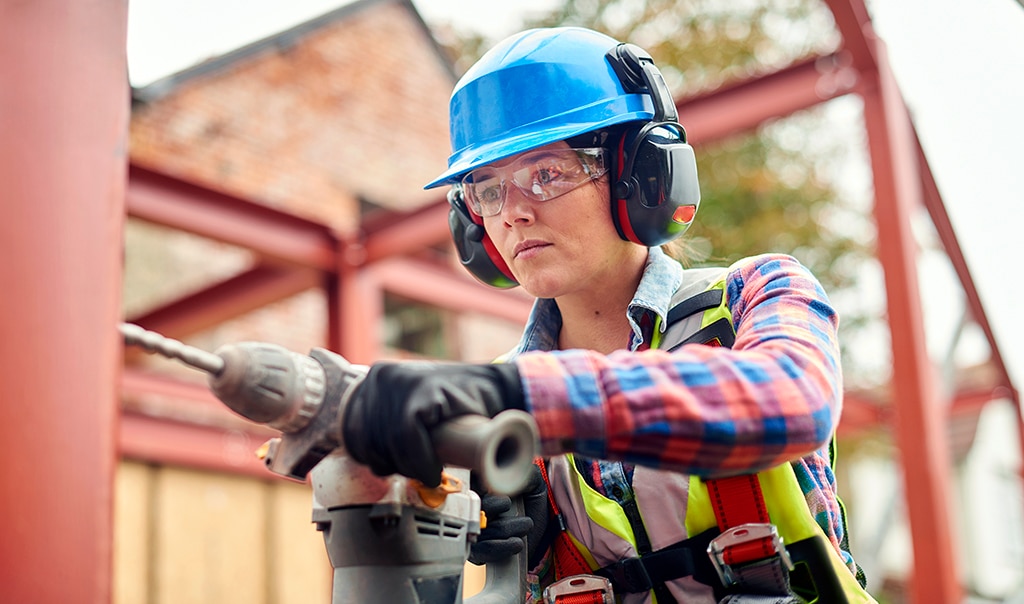 A female construction worker in safety gear drilling on metal