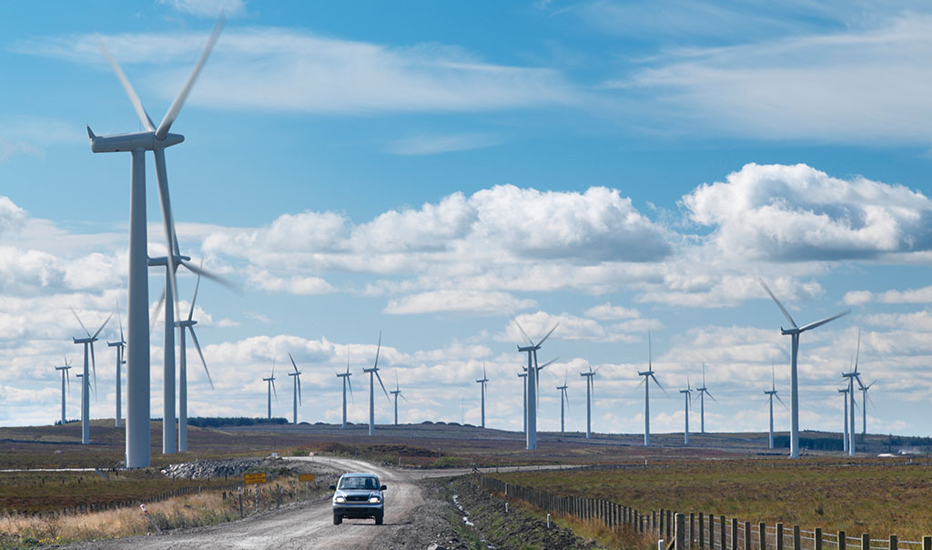 employee driving on road next to wind farm