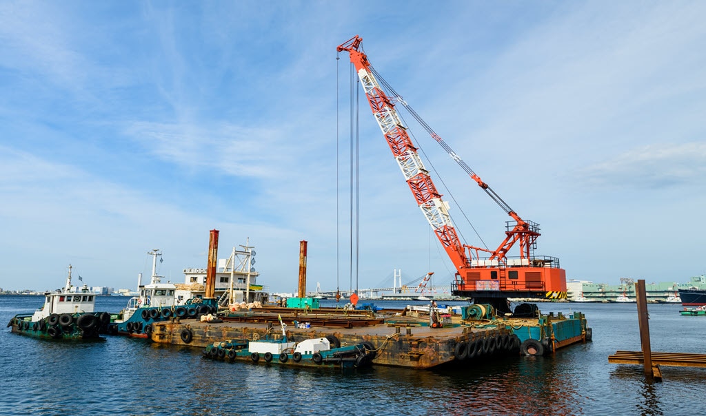 Dredging crane moving heavy equipment on a floating platform.