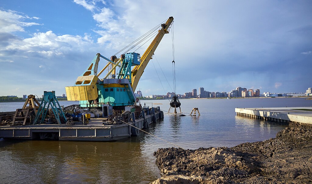 Dredging crane moving debris in water on a floating platform