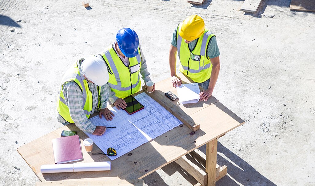 Three construction workers onsite having a meeting and looking at a smart device