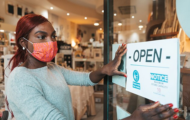 Woman wearing mask placing open sign up at front of business