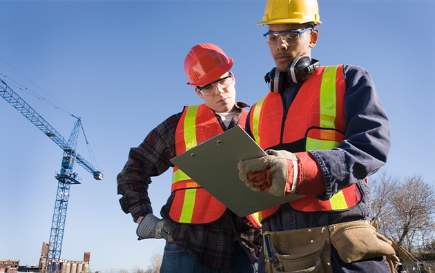 Two construction workers lookin at a clip board. Construction Risk Management During Civil Unrest