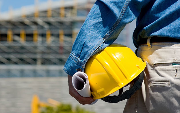 image of man at hip height. He is holding a hard hat against his hip with rolled up plans in his hand, Creating a Safety Culture in the Workplace