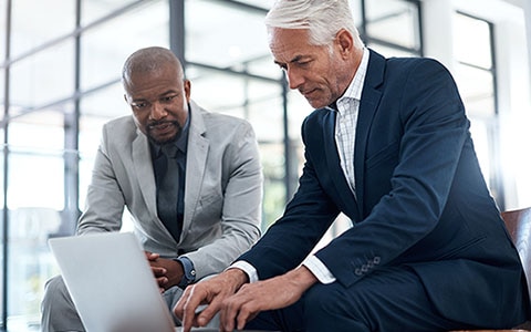 Two senior business managers meeting outside of an office, looking at a laptop computer 