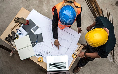 overhead view of two construction site managers or workers studying blueprints