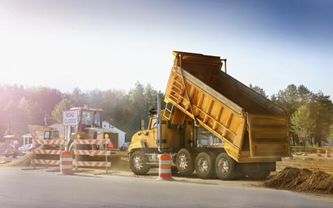 A dump truck next to a construction site dumping dirt