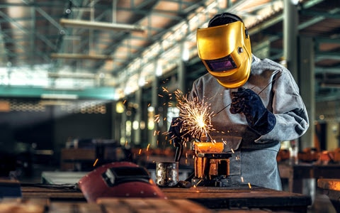 Man in gold mask welding in a factory