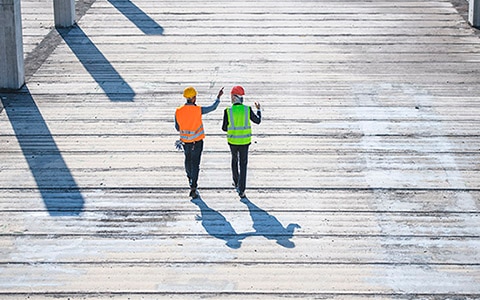 Two construction workers walking along a boardwalk, having a discussion