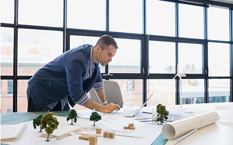 man standing over desk working on laptop, how to choose a professional liability insurance policy for your design firm