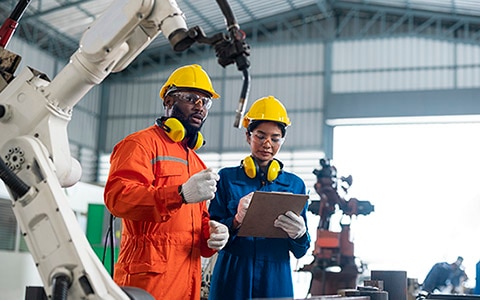 Two workers in a high-tech factory having a discussion, wearing safety gear.