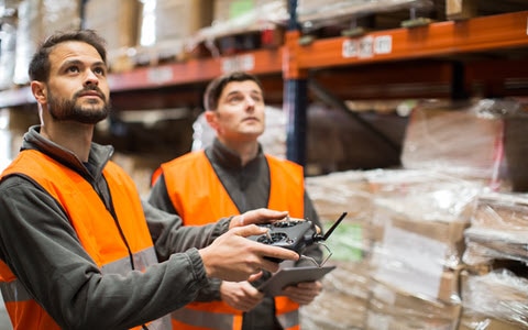 Two workers in warehouse using drone