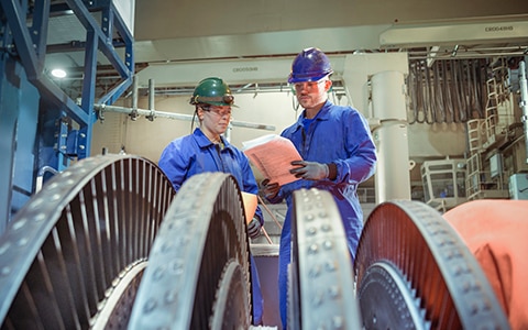 Two technicians examining equipment and machinery inside a factory
