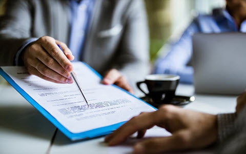 person pointing to a contract with a pen in hand