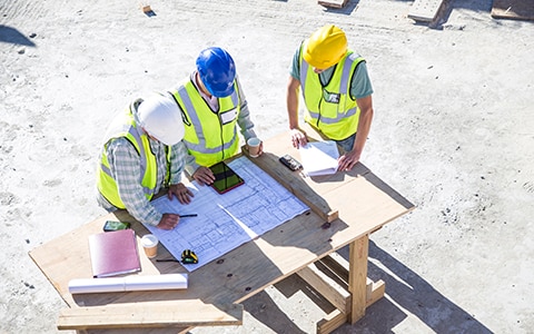 Three construction workers onsite having a meeting and looking at a smart device