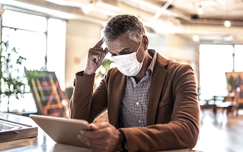 man sits at public place wearing a mask while on his tablet, Establishing and Managing Your COVID-19 Response Plan