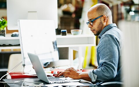 man working at desk looking at two computers. Digital Sales For Online Customer Engagement