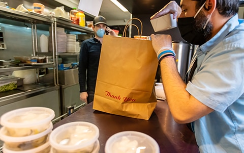 man in mask and gloves at restaurant filling a to go bag, Selling New Products and Services During Recession