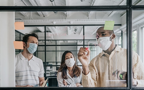 Three people standing in front of a clear writing board writing business things. How to Create Demand for Your Products and Services