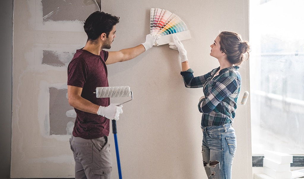 A man and woman looking at a color fan deck next to their house interior wall