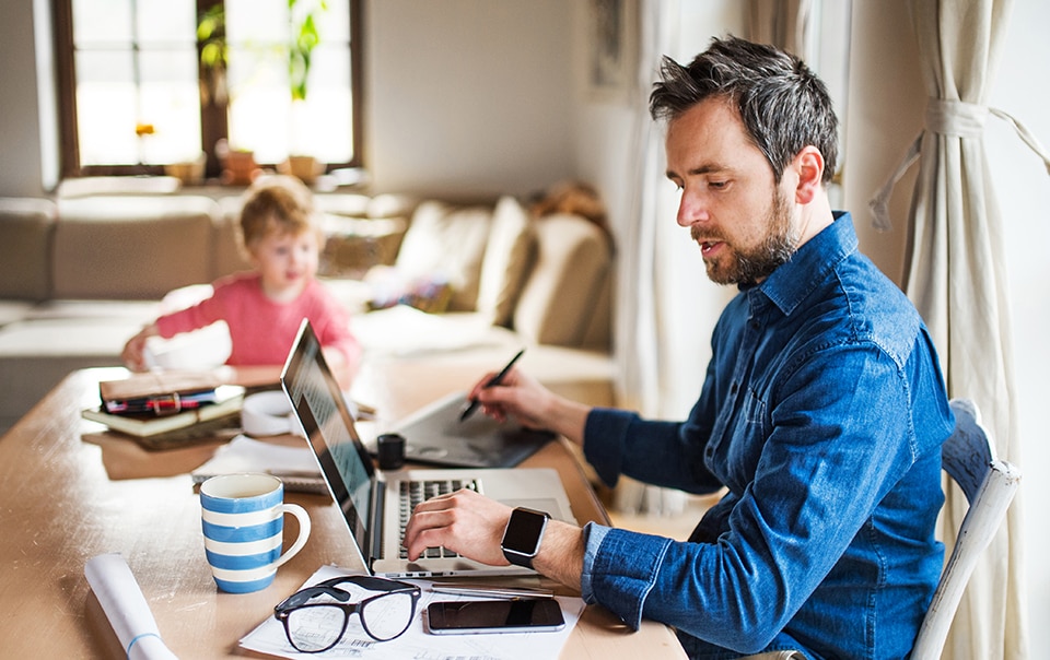 man working on laptop at kitchen table with child also at the table, 6 tips for working from home with your kids
