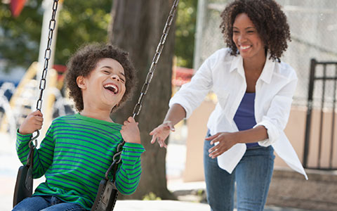 mother pushing son on playset in their backyard