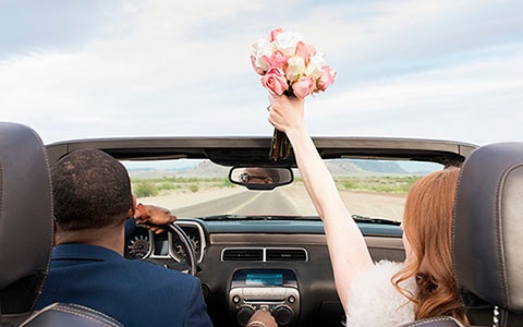 Husband and wife driving off in a convertible car after getting married