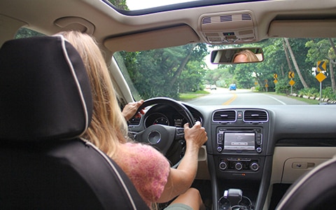 photo taken from back seat of a car of a woman driving a car along with interior, How Telematics Can Help Improve Driver Safety