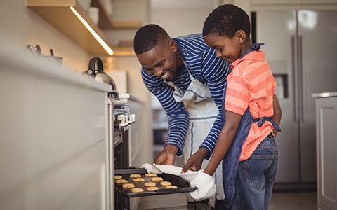 Image of man and son taking cookies out of the oven in their home. Does Homeowners Insurance Cover Appliances?