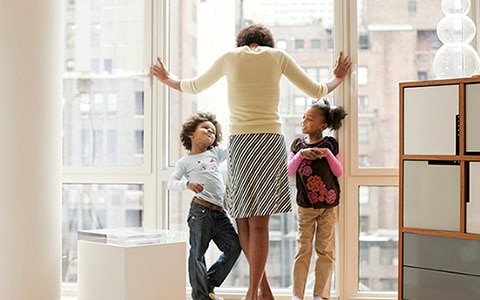 Woman standing with kids looking out window of condo