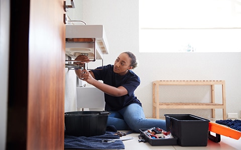 woman tending to pipes under a sink