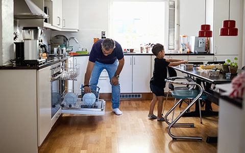 A man putting dishes in the dishwasher and child cleaning the dining table
