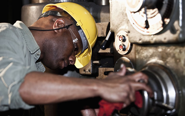 Close up view of an employee in a yellow hard hat and goggles working on machine equipment.